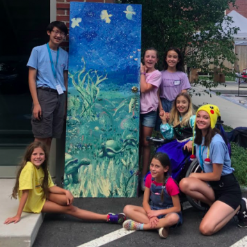 Teen Volunteer Brandon Nguyen stands with group of kids outside next to a door painted with underwater scenes